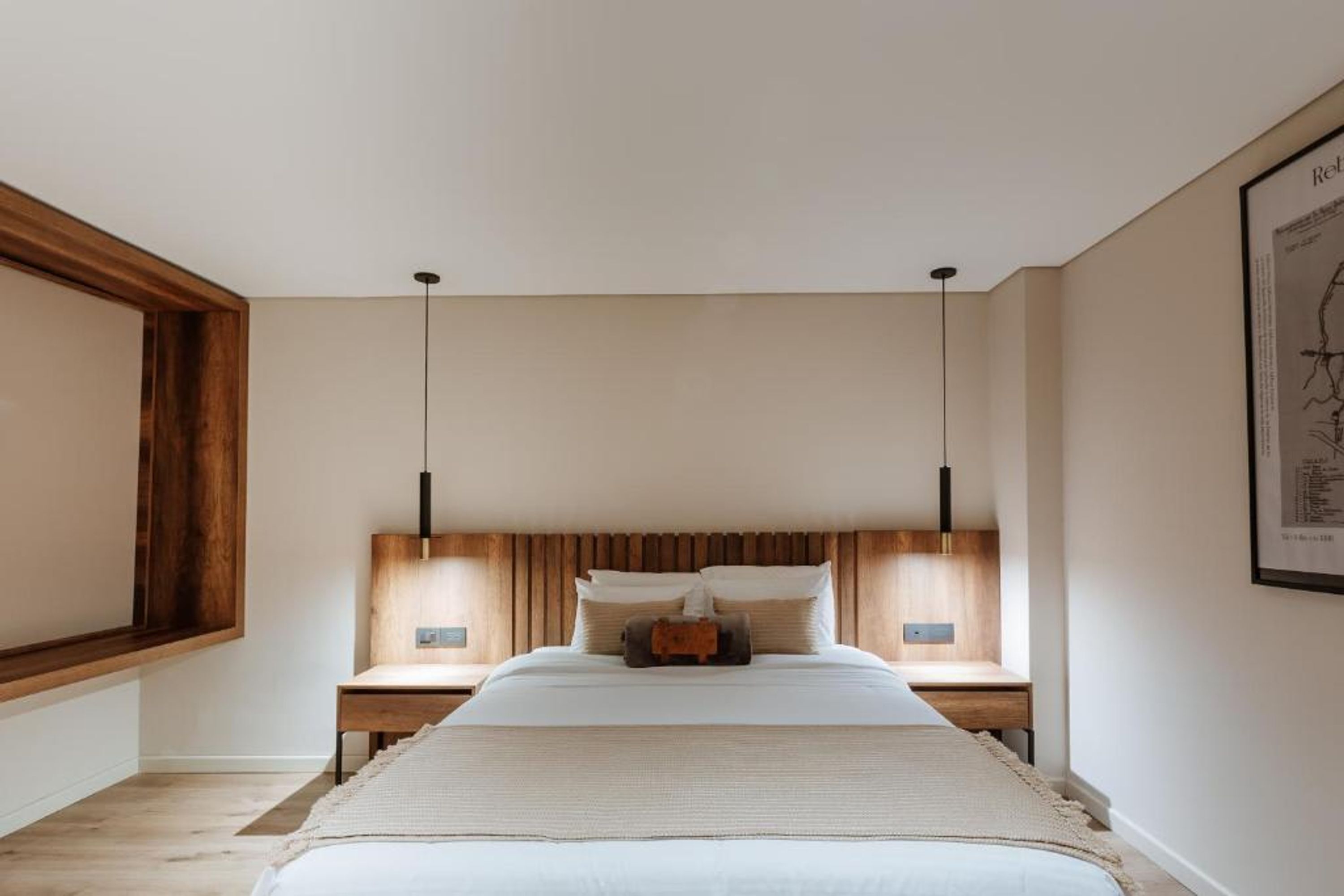A modern bedroom with a large bed, wooden headboard, two bedside tables, and pendant lights.