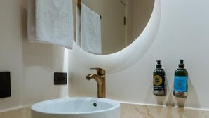 A bathroom with a round mirror, a white sink, and two bottles of hand soap on the countertop. - w Loft Estandar (Medellín)