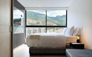 A bedroom with a large window, a bed, a bedside table with a lamp, and a view of a cityscape and mountains. - w Minimalist Loft in Santa Barbara (Bogotá)