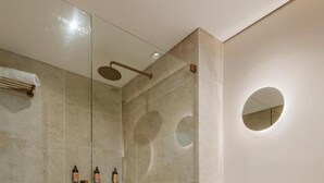 Une salle de bain moderne avec une douche à parois de verre, des toilettes blanches et un meuble-lavabo beige agrémenté d’un miroir.