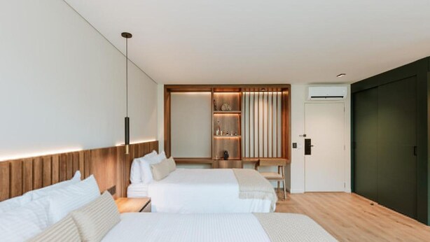 Une chambre d’hôtel moderne avec deux lits, une tête de lit en bois, une armoire intégrée et une table de chevet.