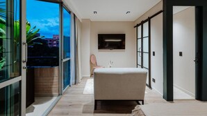 Une chambre d’hôtel moderne dotée d’une grande porte-fenêtre coulissante donnant sur un balcon, d’un lit, d’une petite table et d’un téléviseur fixé au mur.