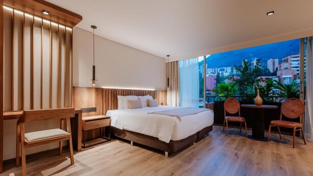 A modern bedroom with a large bed, wooden furniture, a desk, and a view of the city at dusk. - w Loft Superior Mountain (Medellín)