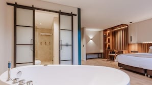 A modern hotel room with a large bathtub, a separate shower area, a bed, and a seating area with a table and chairs. - w Loft Superior Mountain (Medellín)