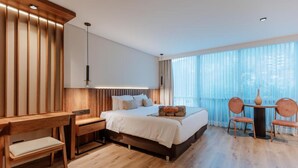 A modern hotel room with a large bed, a desk, and a chair. There is a window with sheer curtains and a view of the city. - w Loft Superior Mountain (Medellín)