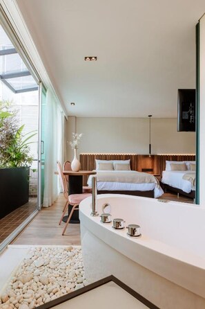 A modern hotel room with a large bathtub, a dining area, and a bedroom with two beds. - w Loft Superior Twin (Medellín)