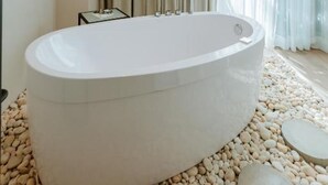 Un baño moderno con una bañera independiente, una mesita pequeña y un ventanal con cortinas.