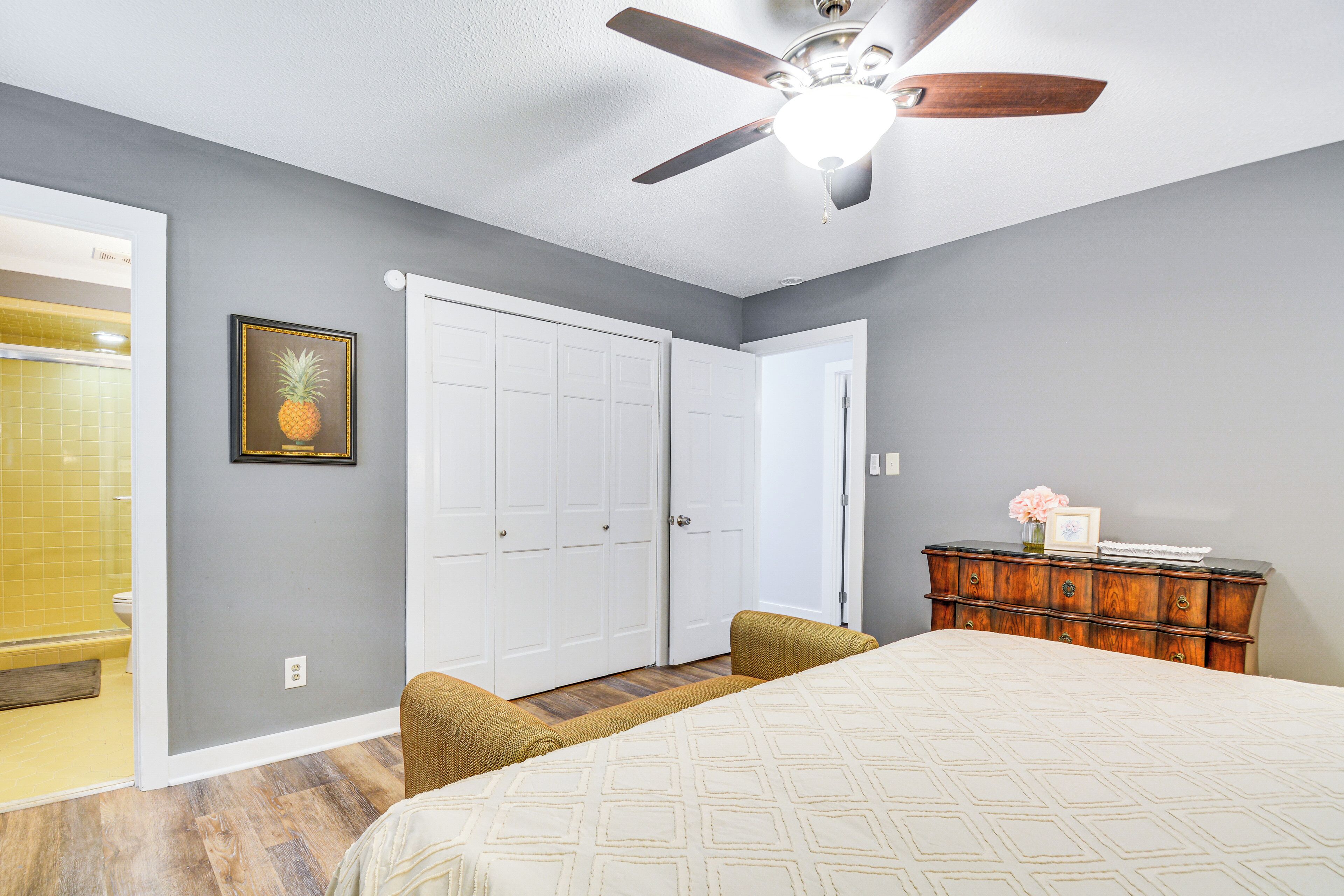 A bedroom with a bed, a ceiling fan, a dresser, and a framed picture on the wall.