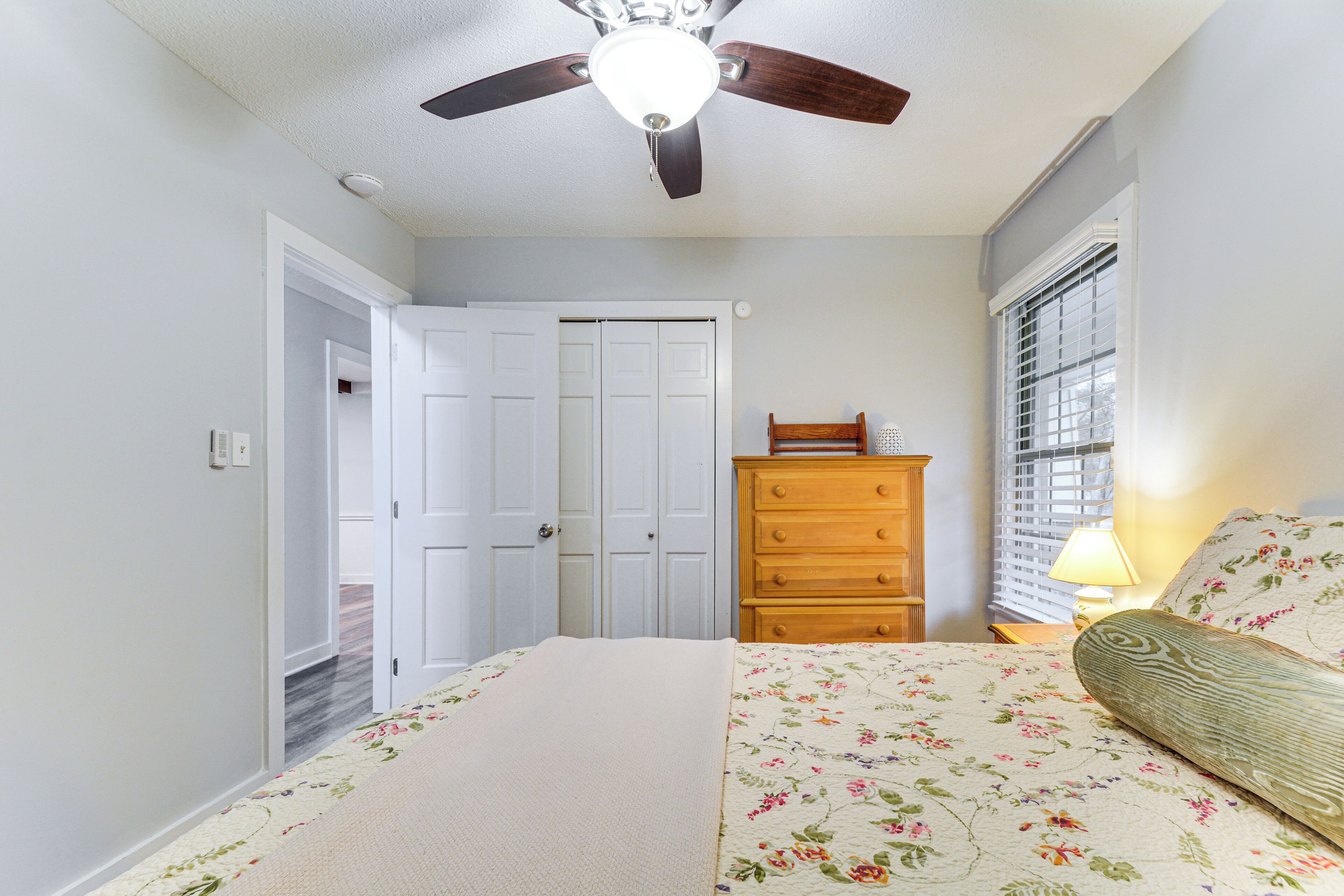 A bedroom with a bed, dresser, ceiling fan, and window with blinds.
