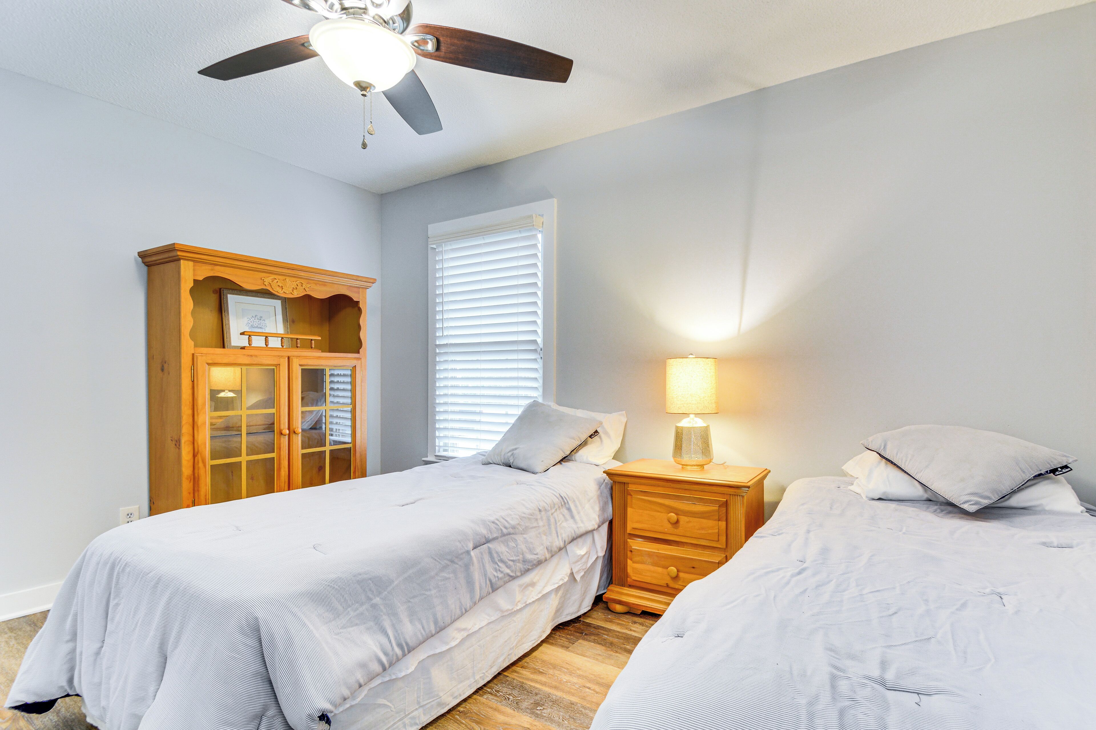 A bedroom with two beds, a wooden wardrobe, a ceiling fan, and a bedside lamp.