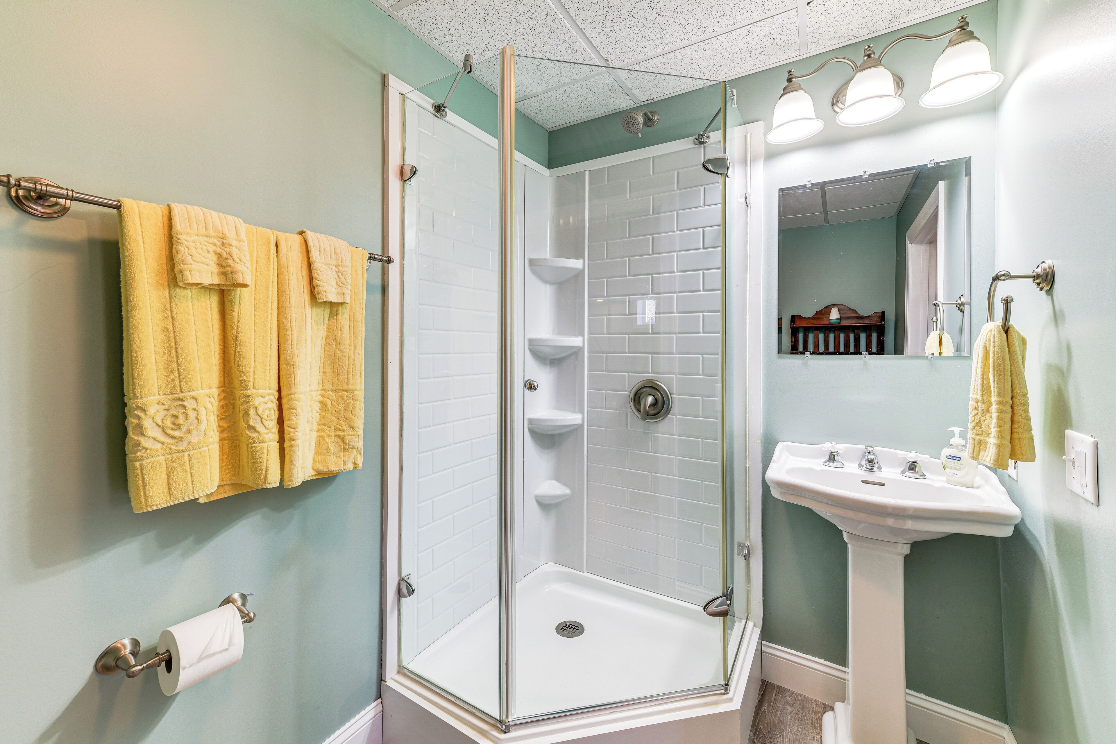 A bathroom with a glass-enclosed shower, a white pedestal sink, and yellow towels on the wall.