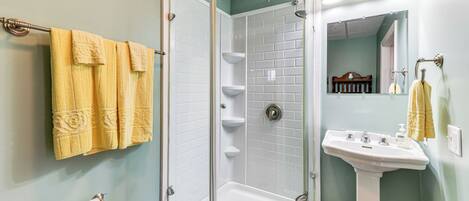 A bathroom with a glass-enclosed shower, a white pedestal sink, and yellow towels on the wall.