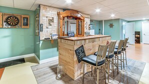 A bar area with a wooden counter, bar stools, and a dartboard on the wall. - Mountain Views & Brook Access: Home in Arkville! (Arkville)