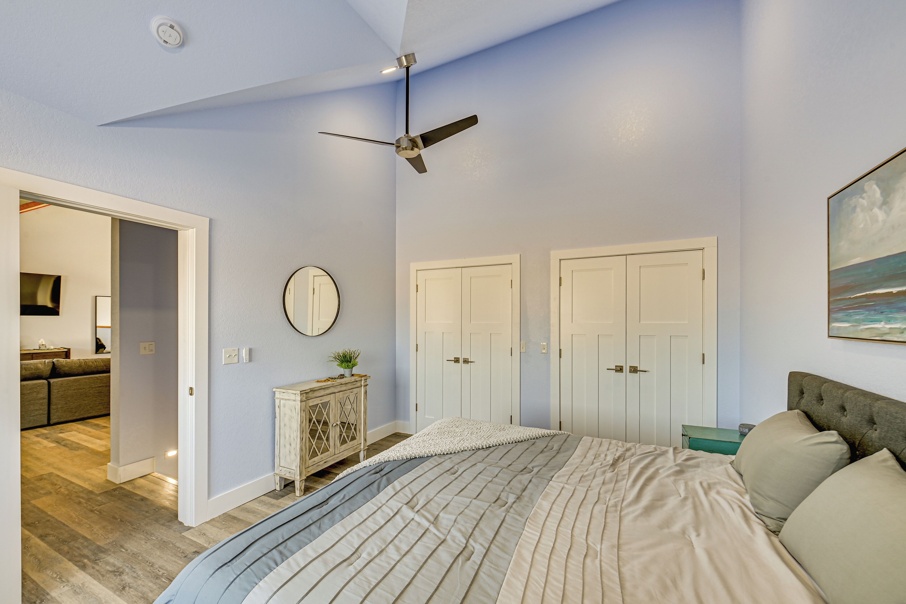 A bedroom with a bed, a ceiling fan, a dresser, a mirror, and two doors.
