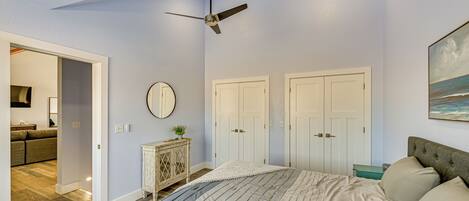 A bedroom with a bed, a ceiling fan, a dresser, a mirror, and two doors.
