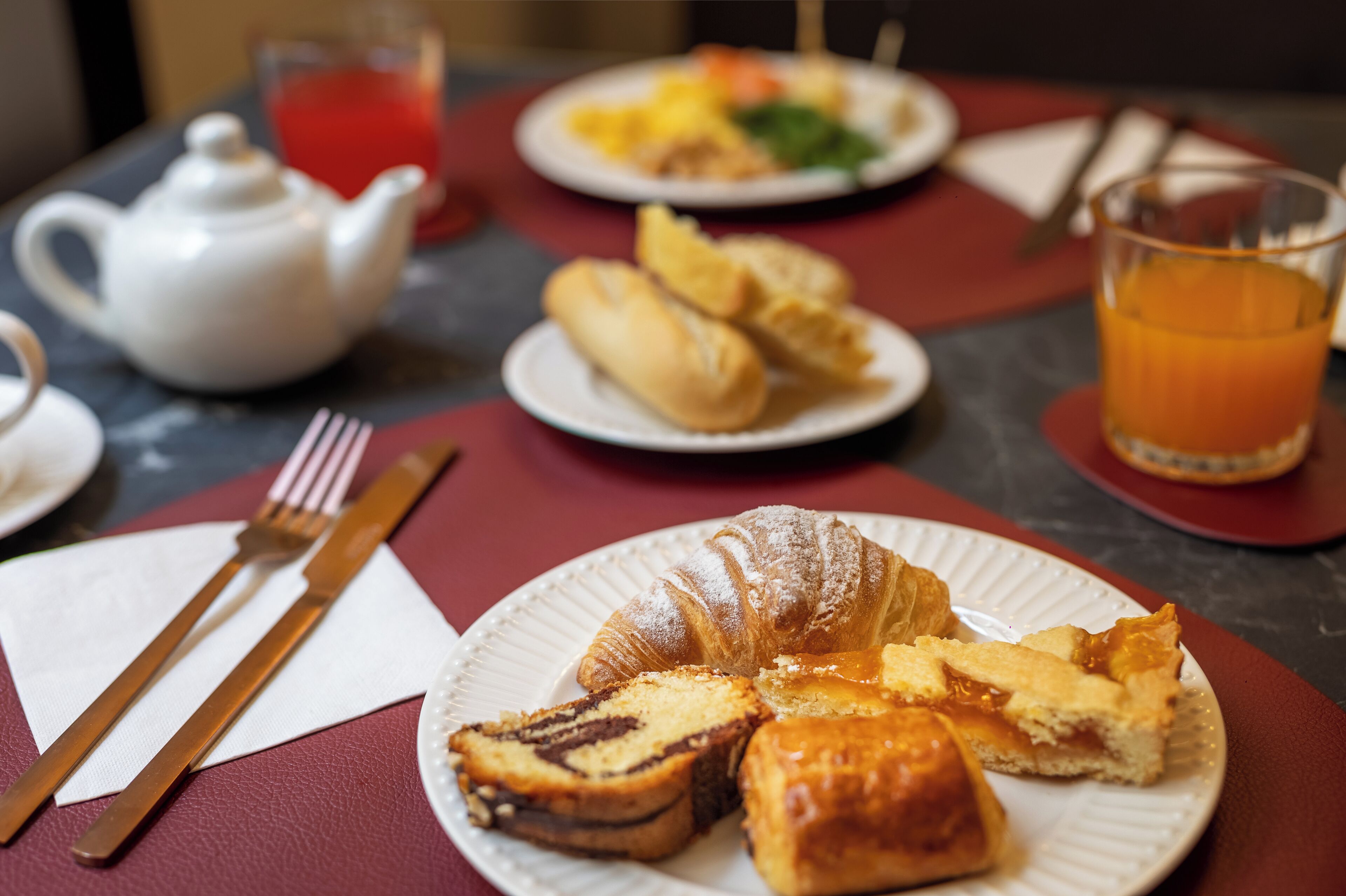 Colazione con un croissant, una fetta di torta e un bicchiere di succo d'arancia su un tavolo.