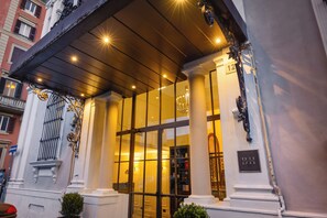 A hotel entrance with large glass doors, columns, and a sign indicating room number 12. - Bh Hotel Dimora D'epoca (Rome)