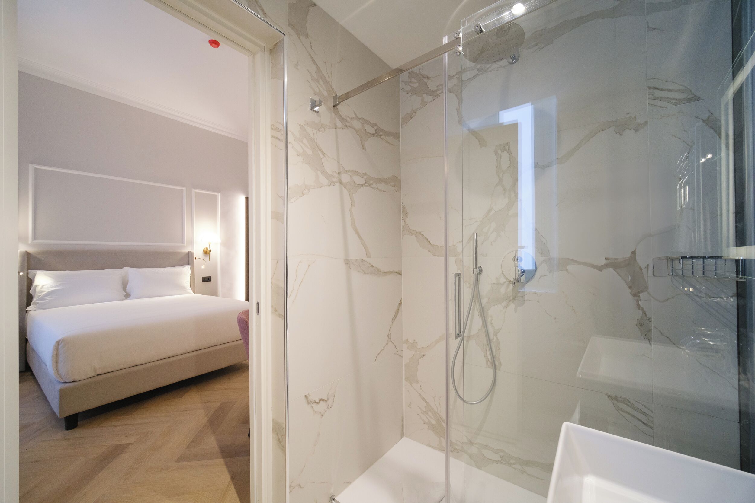 A modern hotel room with a marble shower, a bed, and a white bathroom.