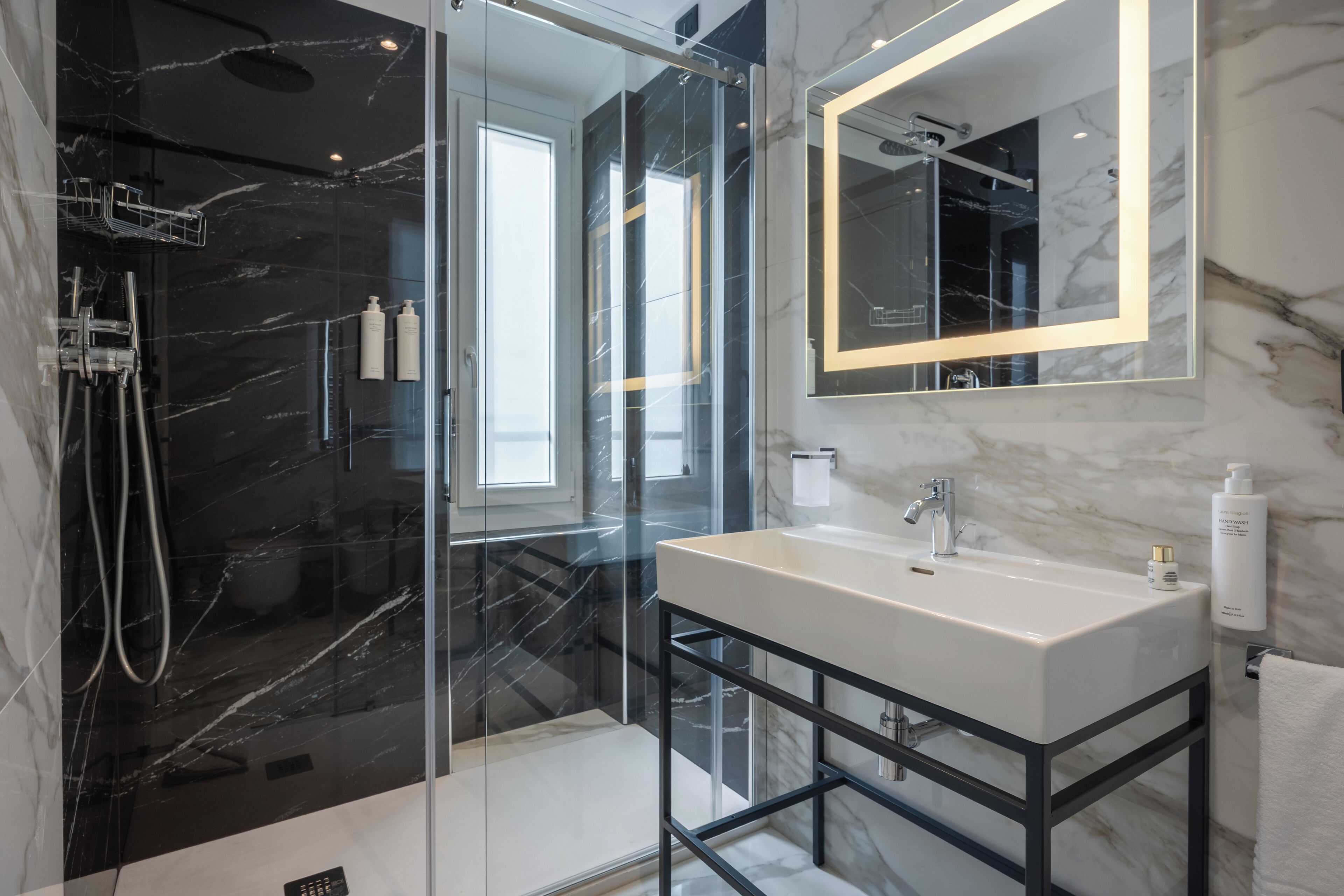 Un bagno moderno con doccia vetrata, parete rivestita in marmo, lavandino bianco e specchio grande.