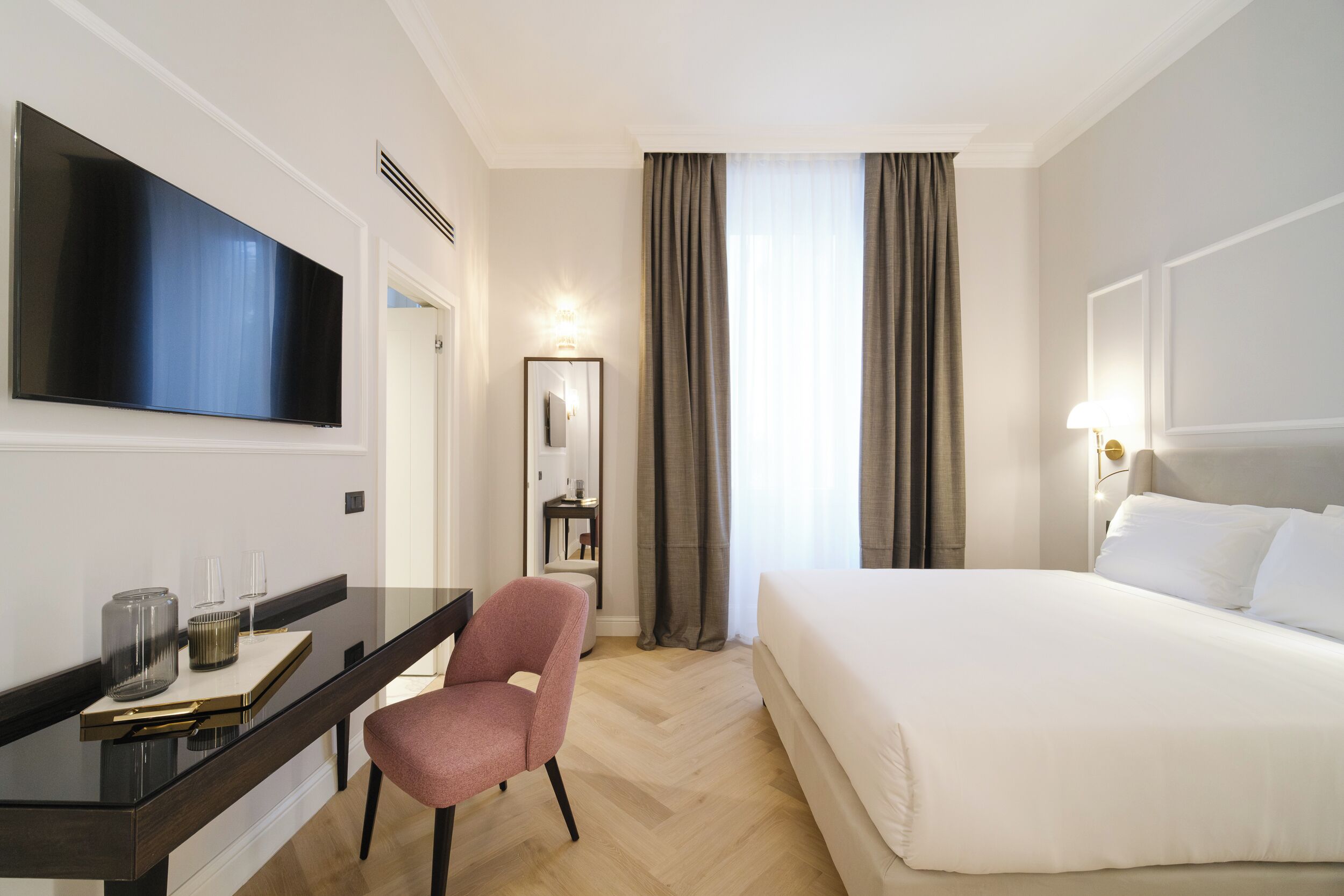 A hotel room with a large bed, a desk with a chair, a flat-screen TV, and a mirror.