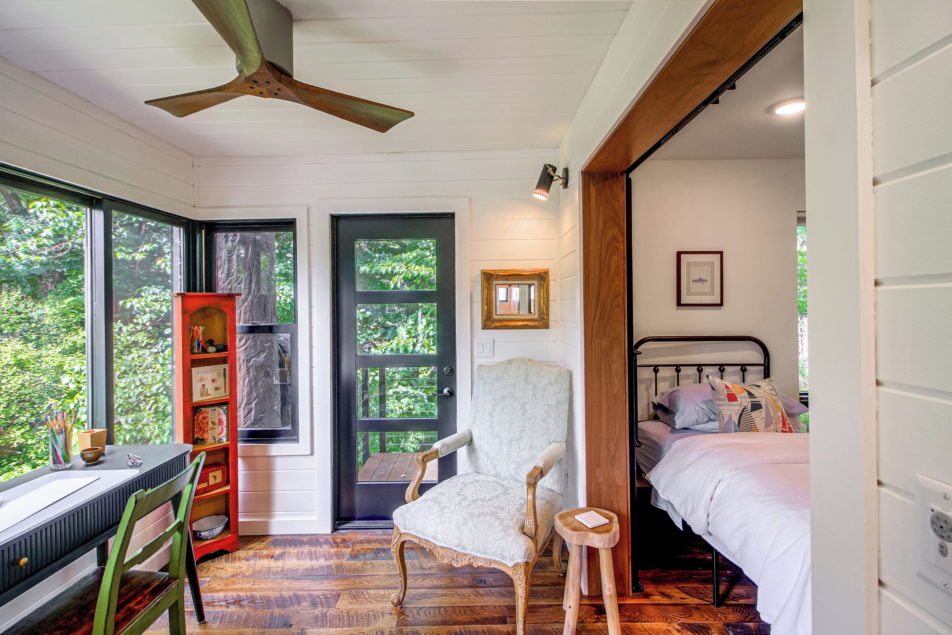 Una habitación con ventilador de techo de madera, un escritorio con silla, una cama con almohadas y una estantería.
