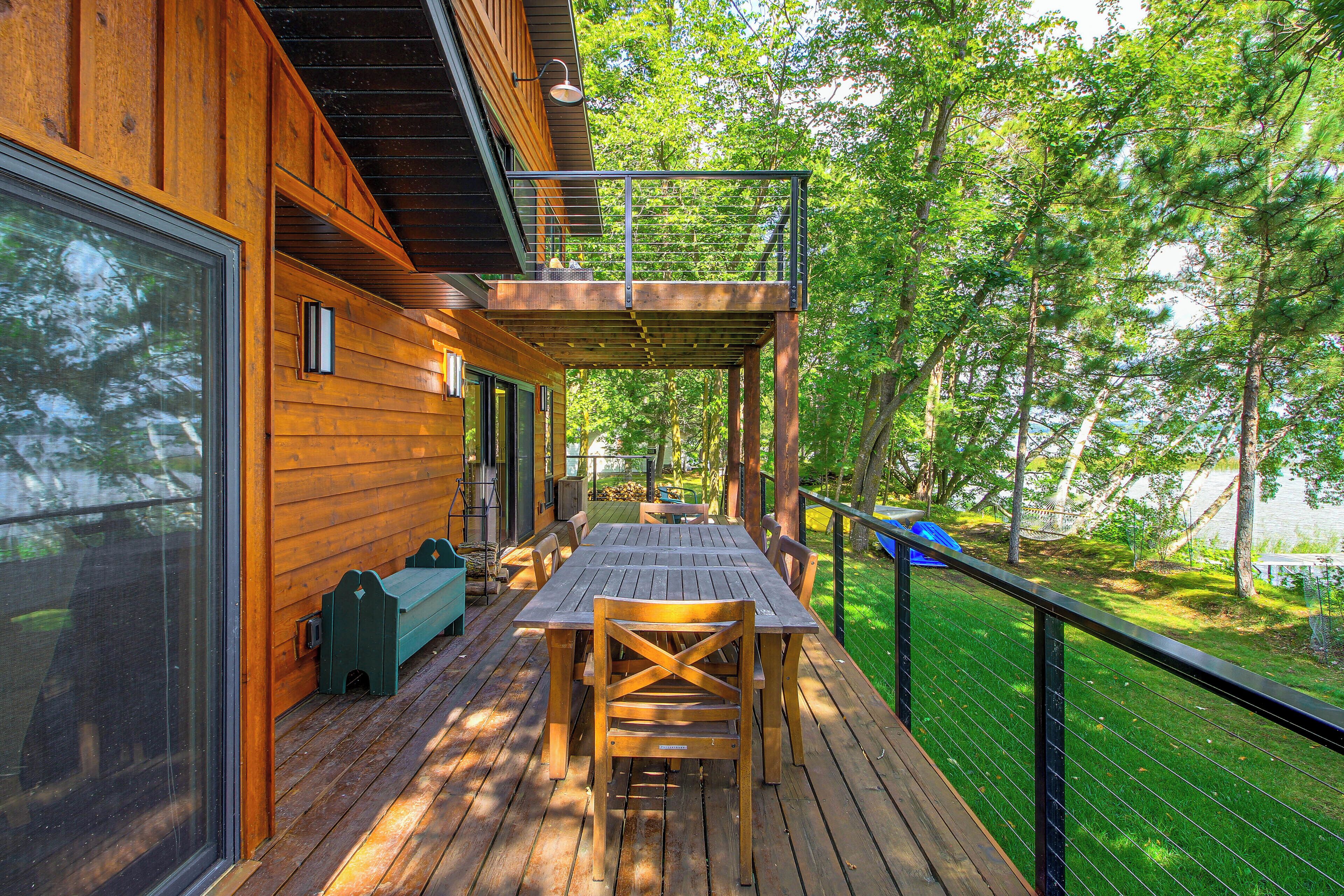 A wooden deck with a table and chairs, overlooking a grassy area with trees.