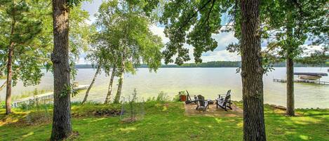 A lakeside view with trees, a dock, and outdoor seating.