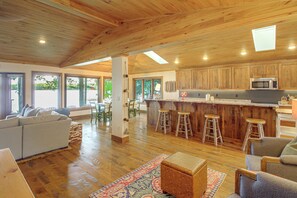 A spacious kitchen with wooden cabinets, a central island with stools, and a dining area with a sofa and chairs. - Short Drive to Itasca State Park - Waterfront Home (Park Rapids)