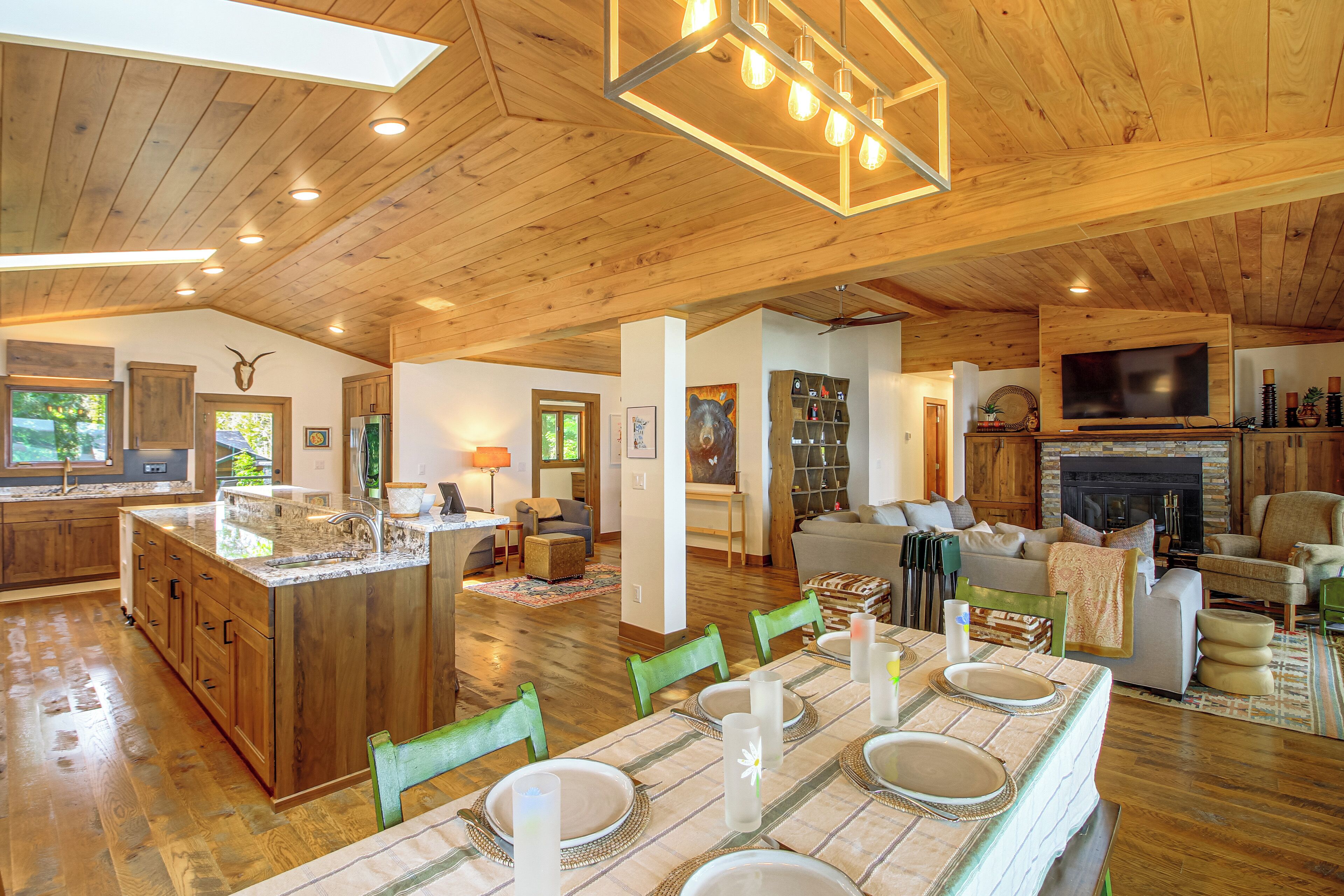 A spacious living area with a wooden ceiling, a fireplace, a television, and a dining area set up for a meal.