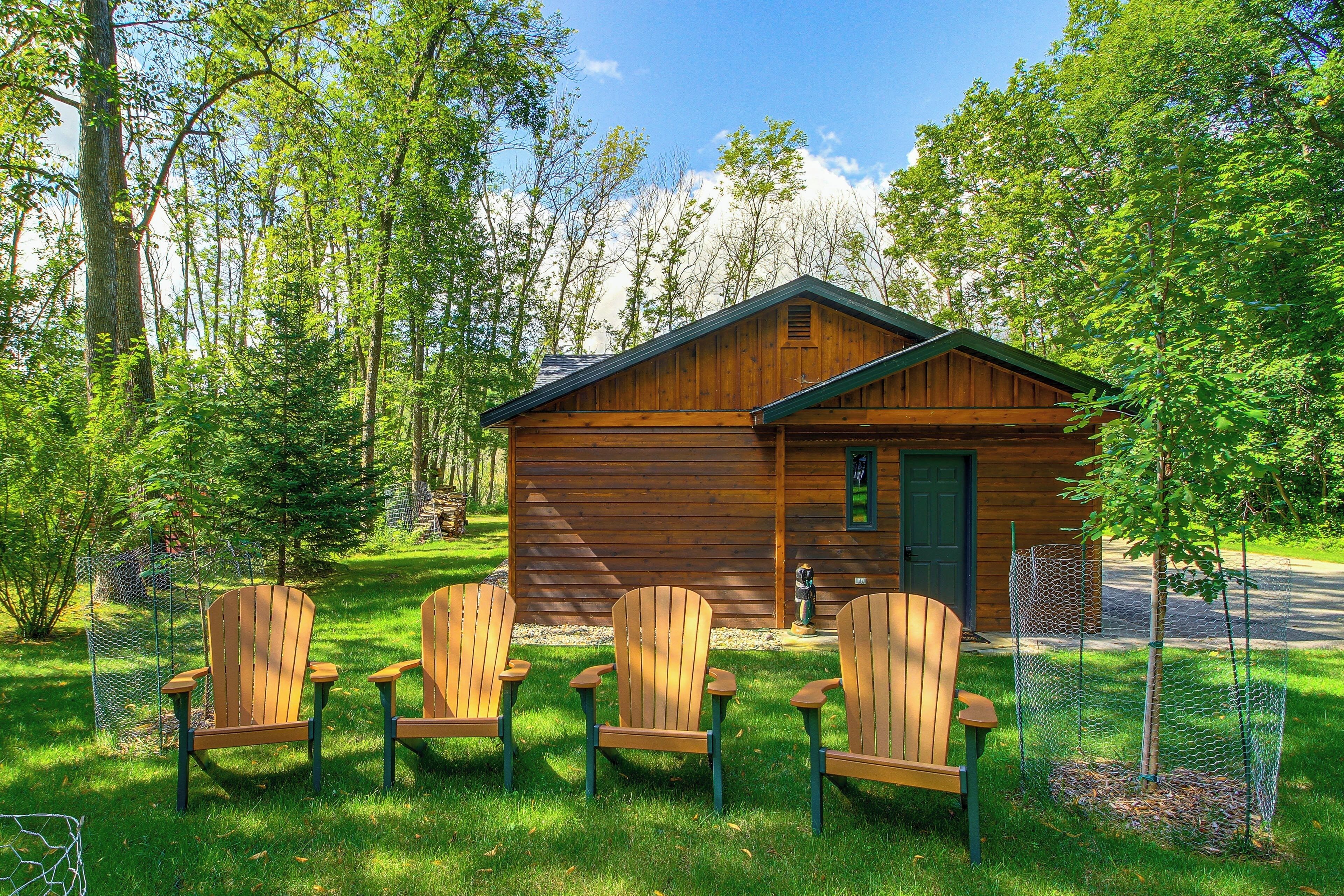 A wooden cabin with a green door, surrounded by a chain-link fence, and three wooden Adirondack chairs in front.