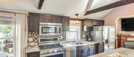A modern kitchen with dark cabinets, stainless steel appliances, and a marble countertop.