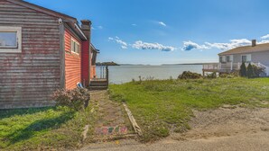 Ein rustikales Holzhaus mit roter Fassade, einer kleinen Veranda und Blick auf einen stillen See.
