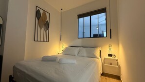 A neatly made bed with white linens and two towels, a bedside table with a lamp, and a wall-mounted picture frame. - M P Beach House in Diano Marina (Diano Marina)