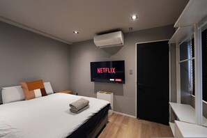 A modern bedroom with a bed, a wall-mounted TV displaying 'NETFLIX', a window with blinds, and a built-in shelf. - Real Life Iidabashi 1-bedroom Cozy 3pax Hi-end (Tokyo)