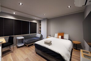 A modern bedroom with a bed, a desk, a chair, a sofa, and a window with blinds. - Real Life Iidabashi 1-bedroom Cozy 3pax Hi-end (Tokyo)