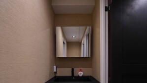 A narrow hallway with a mirror reflecting a door and a light fixture. A black sink with a soap dispenser is visible. - Real Life Iidabashi 1-bedroom Cozy 3pax Hi-end (Tokyo)