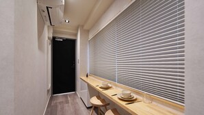 A narrow hallway with a wooden counter and two stools, a window with blinds, and a door leading to another room. - Real Life Iidabashi 1-bedroom Cozy 3pax Hi-end (Tokyo)