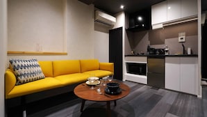 Ein gemütlicher Wohnraum mit einem gelben Sofa, einem runden Holztisch und einer Küchenzeile.