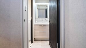 A narrow hallway leading to a bathroom with a mirror, a sink, and a cabinet. - Real Life Iidabashi 1-bedroom Luxe 3mins to Subway (Tokyo)