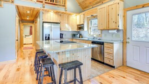 A modern kitchen with wooden cabinets, a central island with stools, a built-in oven, and a microwave.