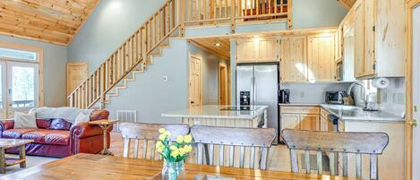 A spacious living area with a wooden staircase, a kitchen with wooden cabinets, and a dining table with a vase of flowers.