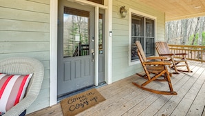 A porch with a wooden door, rocking chairs, and a doormat.