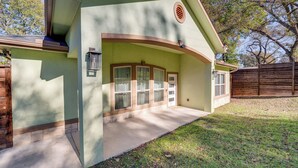Uma casa com fachada verde, varanda frontal e cerca de madeira ao fundo.