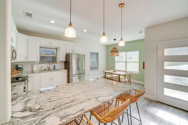A spacious kitchen with white cabinets, a large island, and a dining area with wicker chairs. - 10 Mi to Dtwn Dallas: Chic Home w/ Yard! (Dallas)