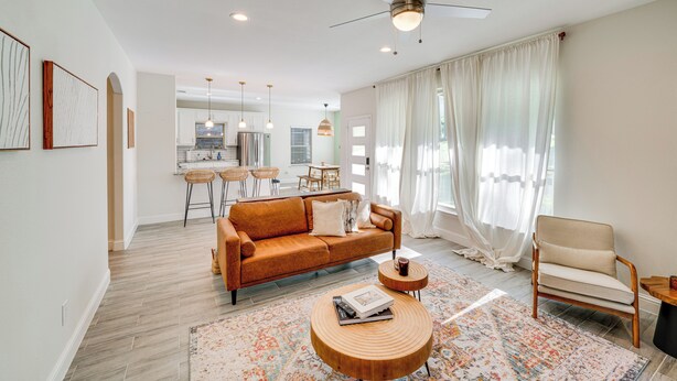 Uma sala de estar moderna com sofá, poltrona e mesa de centro. Ao fundo, uma área de jantar com cozinha visível.