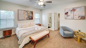Um quarto com cama, um banco, uma cadeira, ventoinha no teto e obras de arte nas paredes.