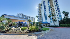 A modern hotel with a pool area, palm trees, and a large building in the background. - Walk to White-sand Beach: Resort Condo in Destin! (Destin)