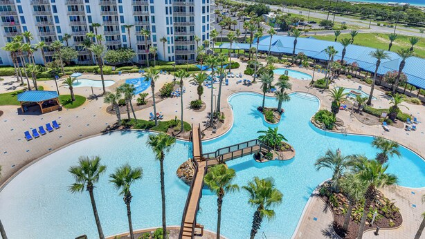 A resort with multiple swimming pools, palm trees, and a large building in the background. - Walk to White-sand Beach: Resort Condo in Destin! (Destin)