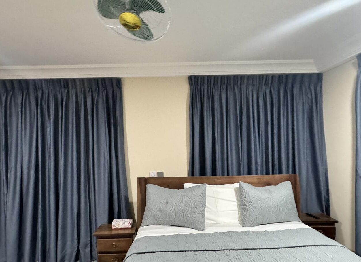 A bedroom with a bed, wooden headboard, two bedside tables, a nightstand, and a ceiling fan.