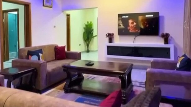 Un soggiorno moderno con ventilatore a soffitto, televisione a schermo piatto montata su una parete bianca, divano, tavolino da caffè e una pianta in vaso.